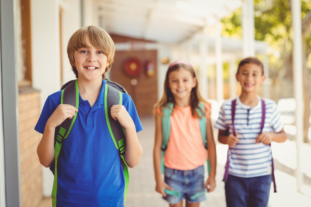 three kids with backpacks standing in school hallway